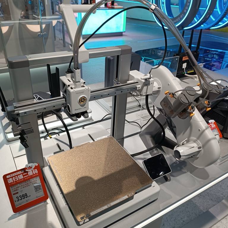 A Bambu Lab A1 on a store display: the open frame, the toolhead on the X-axis rail with filament tubes looping in from above, and a textured PEI plate on the bed