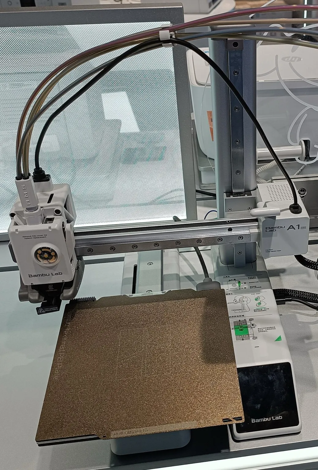 A Bambu Lab A1 mini on a store display: the toolhead with filament tubes plugged in on the X gantry, a textured PEI plate on the bed, the touchscreen and the A1 mini label on the Z column