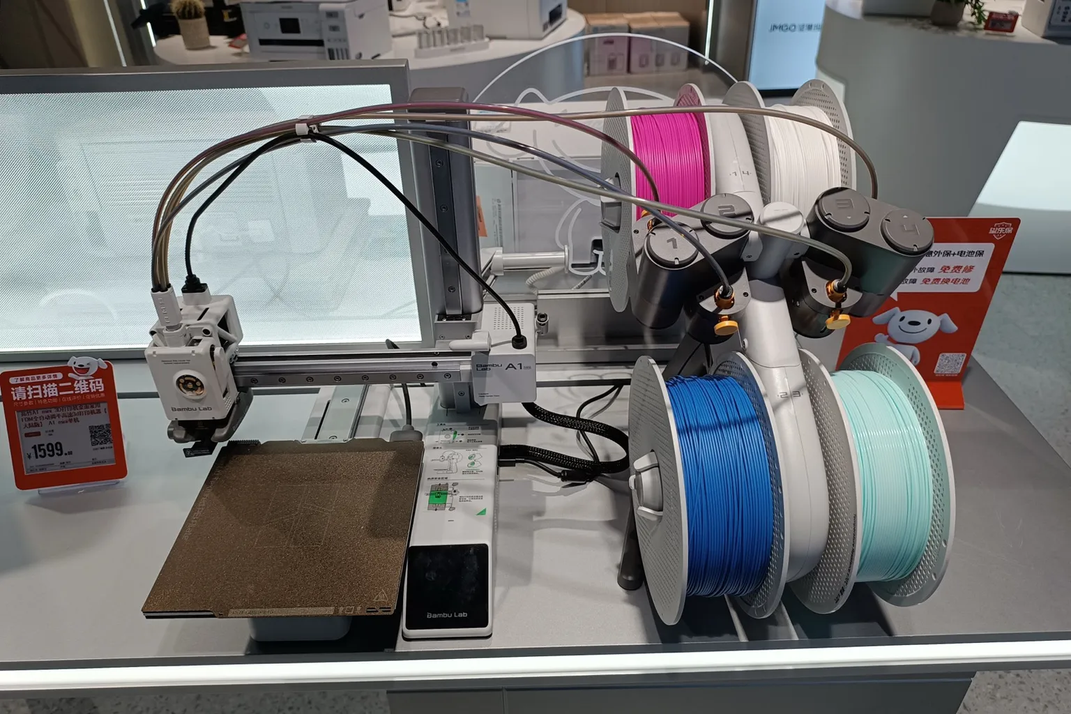 A Bambu Lab A1 mini with an AMS lite holding pink, white, blue and mint filament spools on a store display table