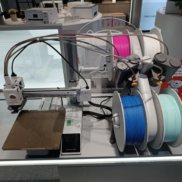 A Bambu Lab A1 mini with an AMS lite holding pink, white, blue and mint filament spools on a store display table