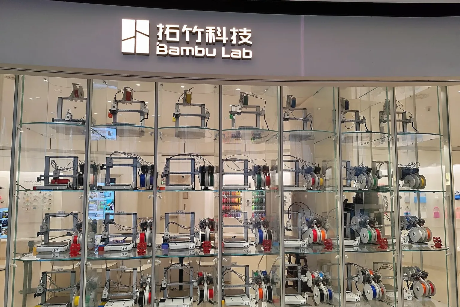 Rows of Bambu Lab printers running behind the glass front of a Bambu Lab store