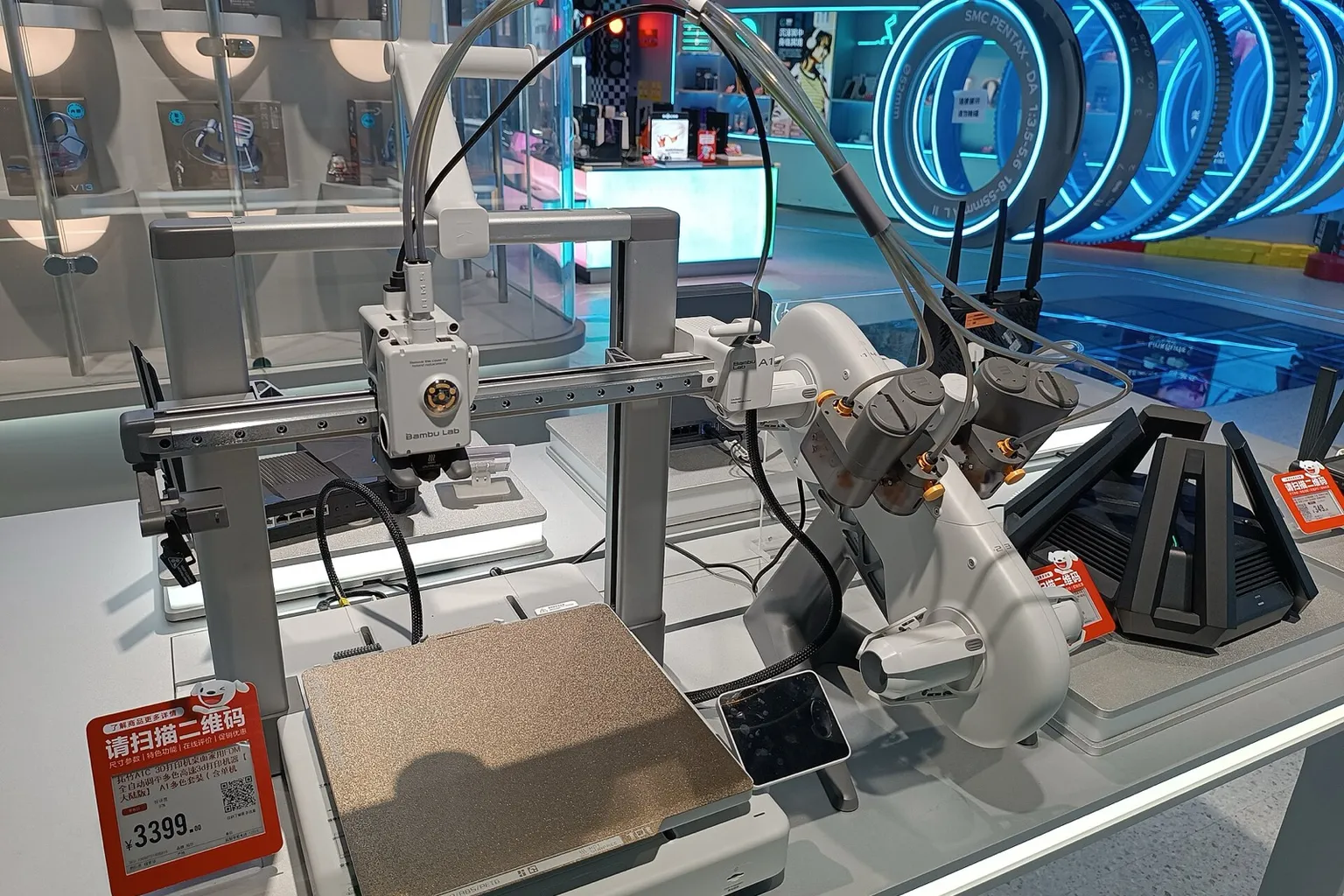 A Bambu Lab A1 with an AMS lite on a store display table, with Wi-Fi routers on the table behind and to the right of it