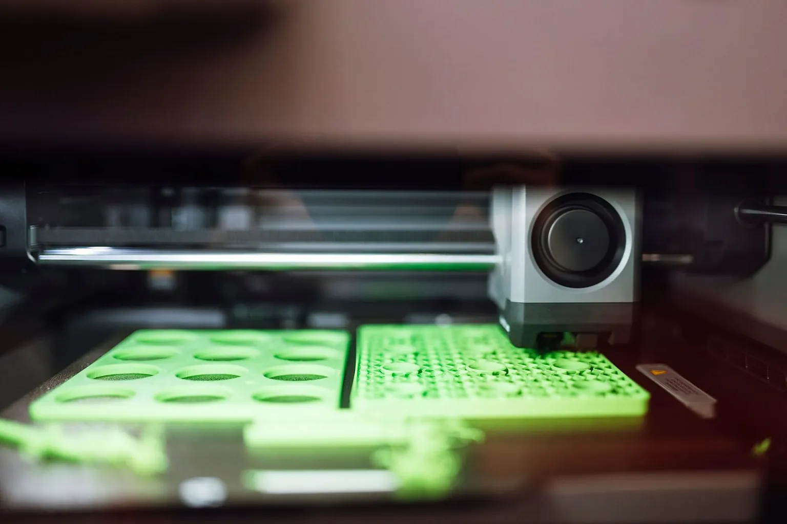 A Bambu Lab toolhead printing green parts on the build plate
