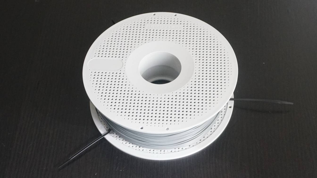 A white Bambu Lab reusable spool wound with gray filament, lying on a black surface