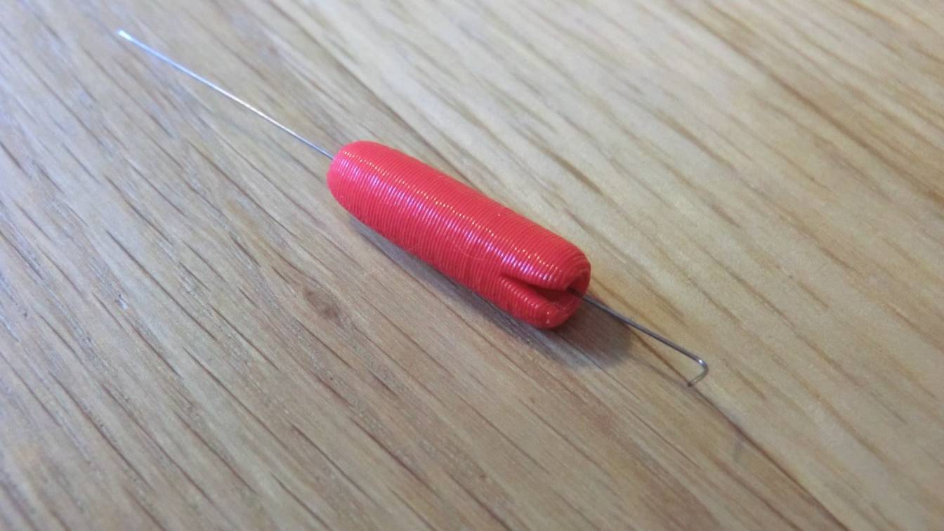 A thin steel nozzle-cleaning needle set in a red 3D-printed handle, lying on a wooden table