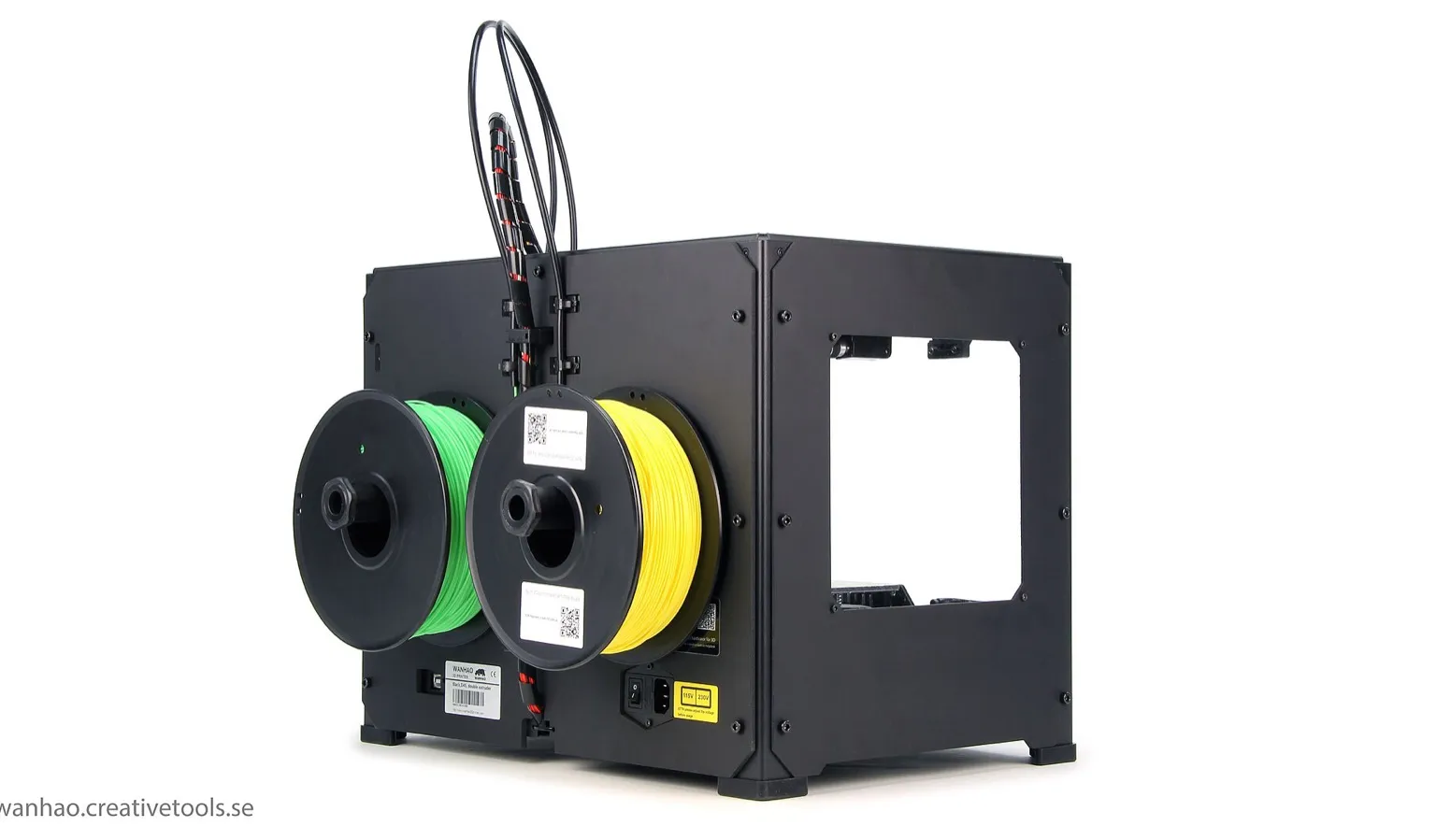 A black steel-framed desktop 3D printer seen from the back, with a green and a yellow filament spool mounted side by side and two feed tubes running over the top