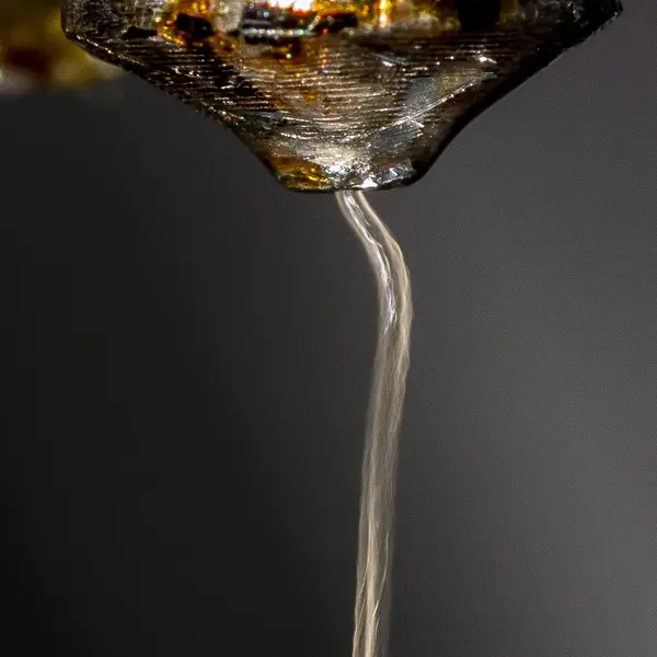 Close-up of a 3D printer nozzle with a thin strand of molten plastic hanging from its tip