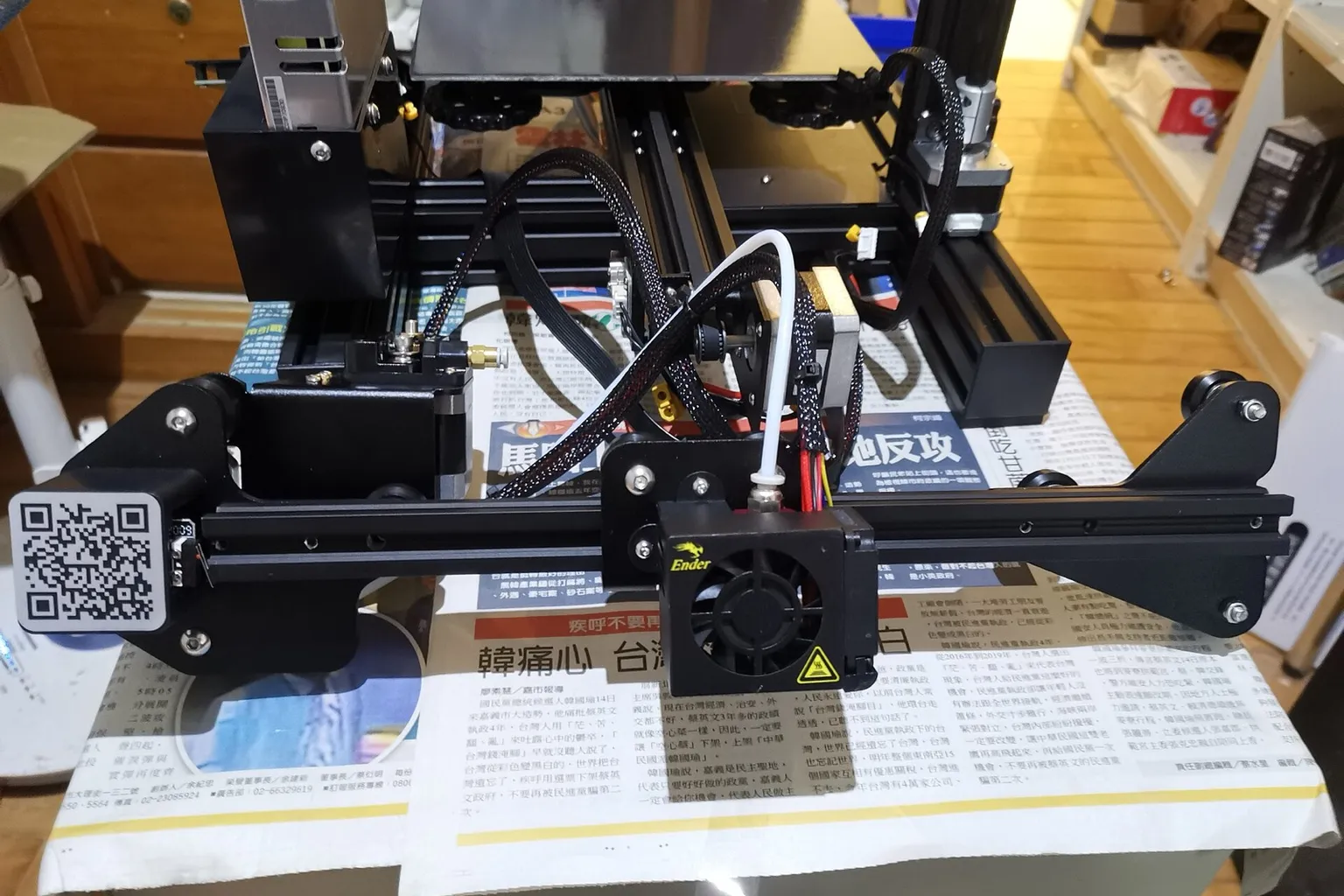 The X gantry of a Creality Ender 3 during kit assembly, with the stock Bowden extruder at its left end and a white PTFE tube rising from the hotend under the fan shroud on the carriage