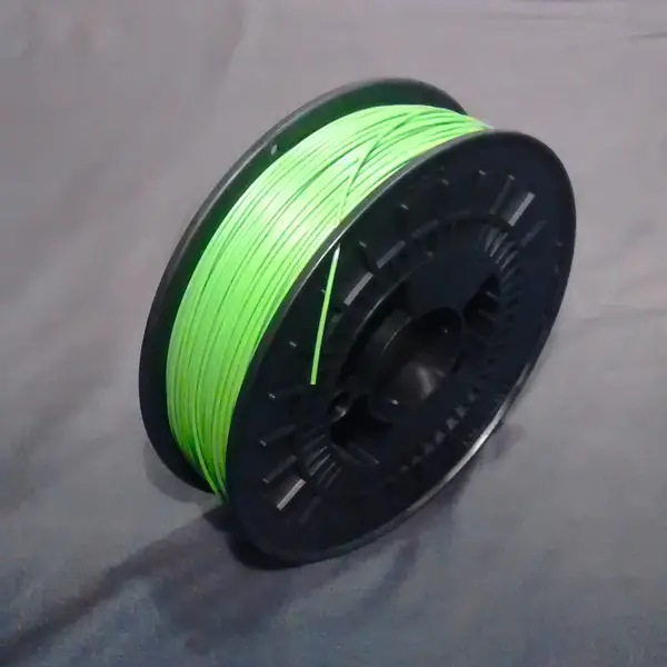 A spool of light green ABS filament on a black plastic reel, lying on a grey cloth