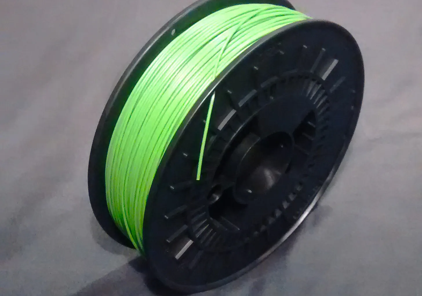 A spool of light green ABS filament on a black plastic reel, lying on a grey cloth
