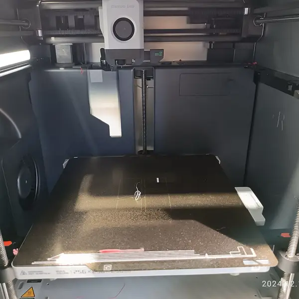 Inside an enclosed Bambu Lab printer on a showroom floor: a single-nozzle toolhead on the gantry above an empty textured build plate with a build-volume label on its front edge