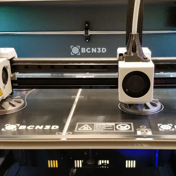 Two independent print heads with white fan shrouds parked side by side over a BCN3D build plate
