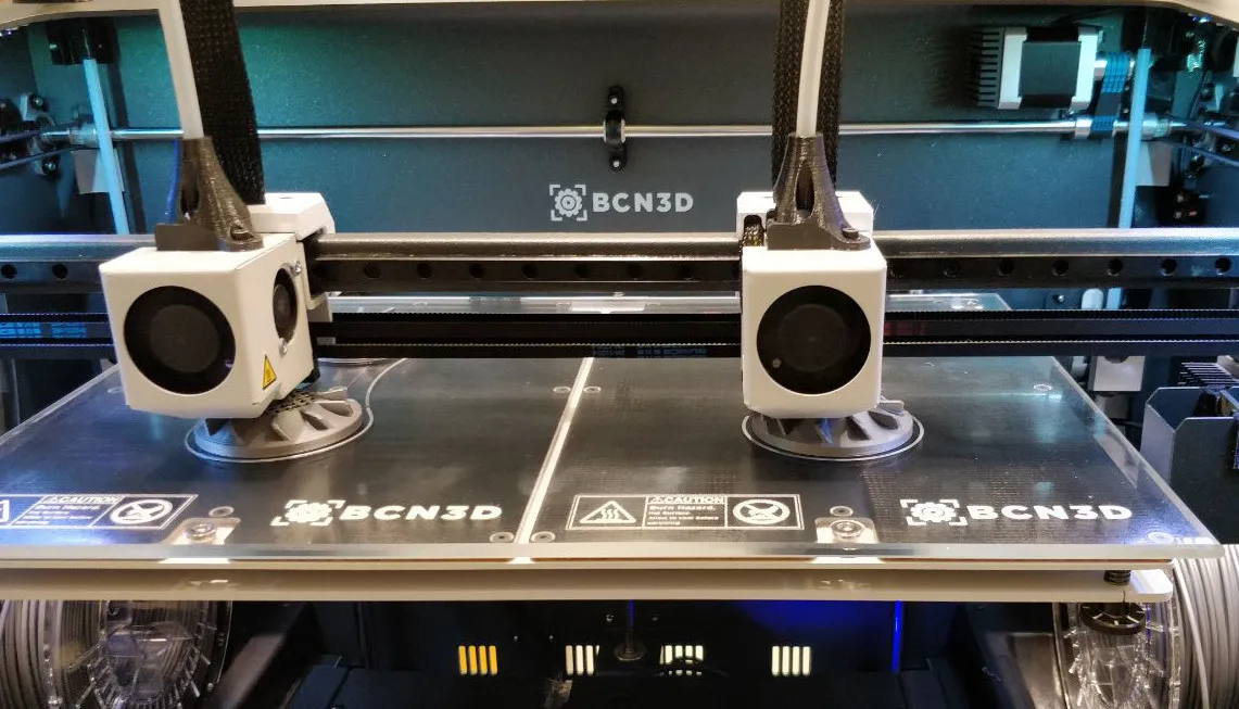 Two independent print heads with white fan shrouds parked side by side over a BCN3D build plate
