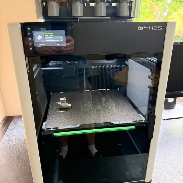 A Bambu Lab H2S printer with an AMS unit on top and a printed boat on its build plate