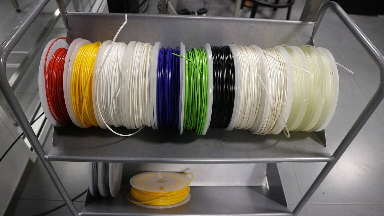 A cart holding a row of filament spools in red, yellow, white, blue, green and black