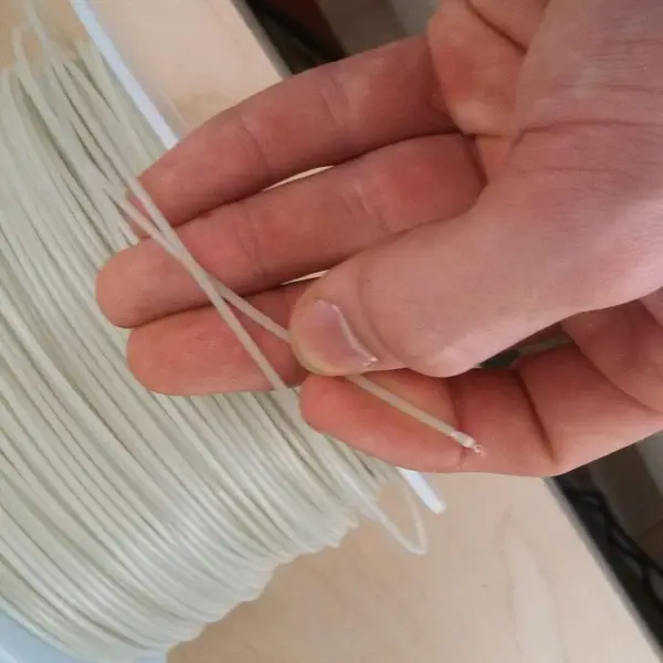 A hand pulling a loose strand of white filament off a spool