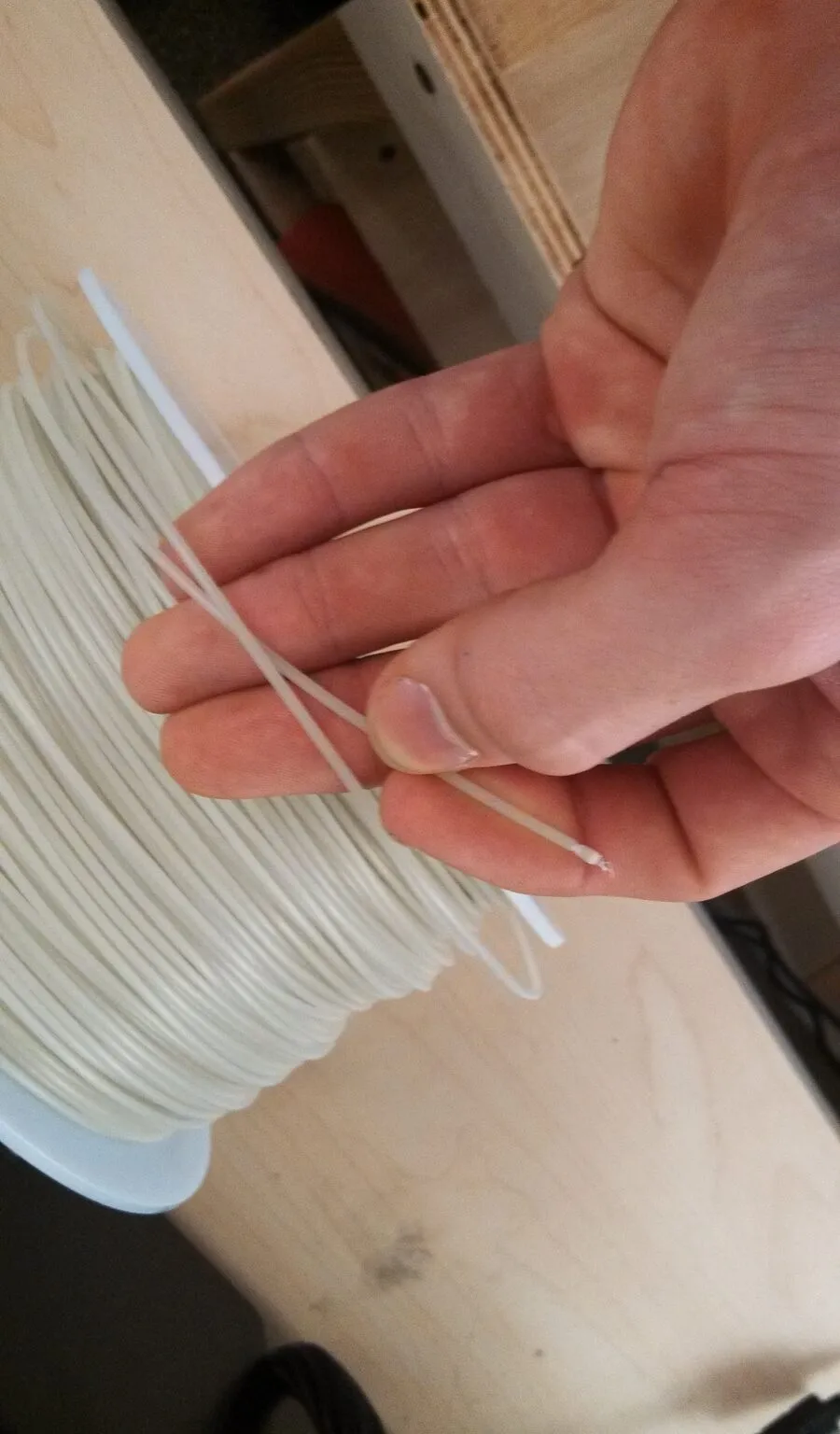 A hand pulling a loose strand of white filament off a spool