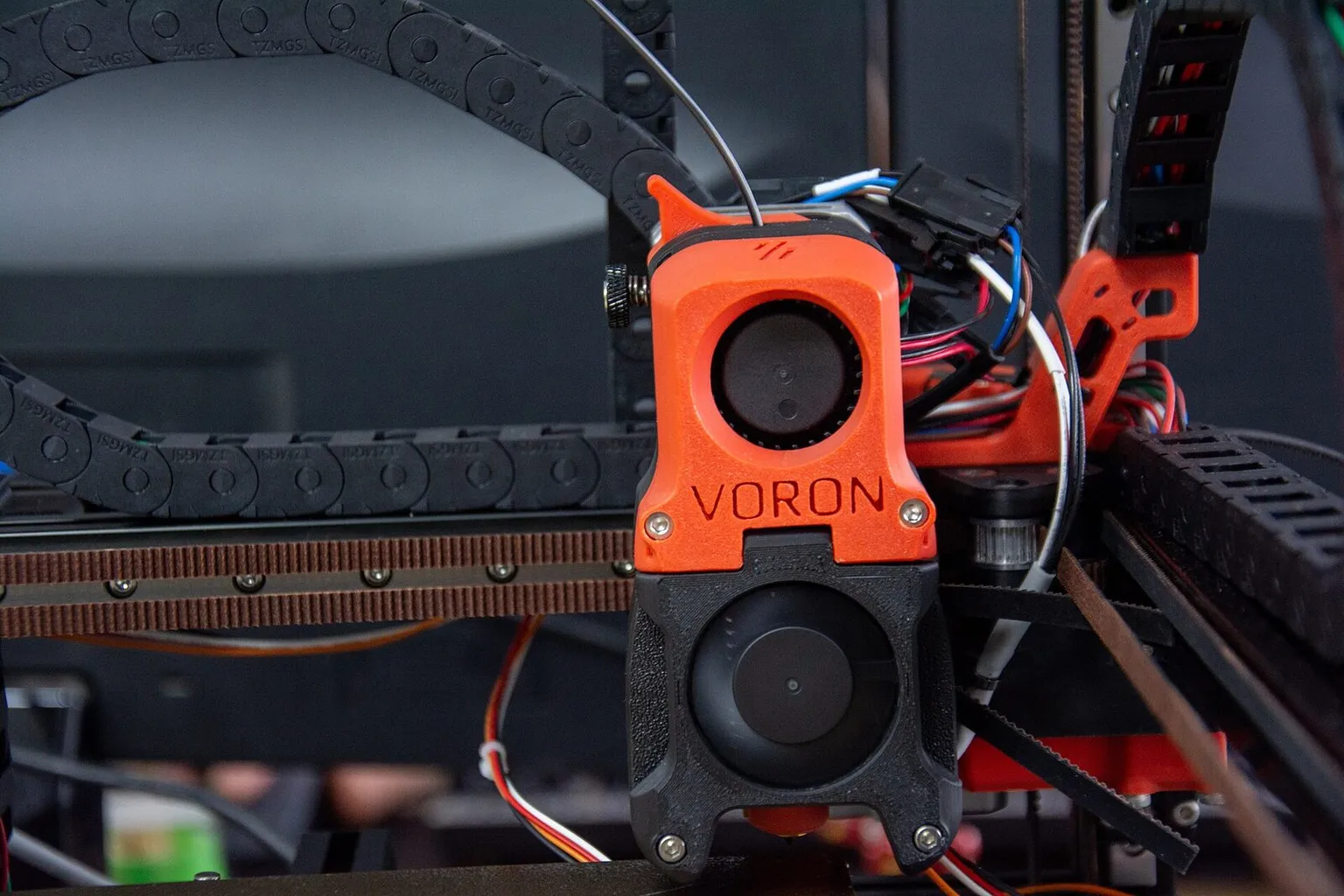 Front view of an orange Voron toolhead on its gantry, with the cable chain behind it