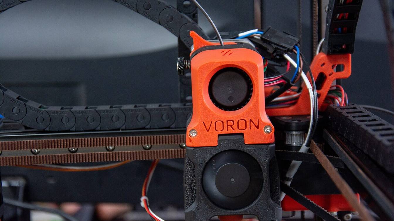Front view of an orange Voron toolhead on its gantry, with the cable chain behind it