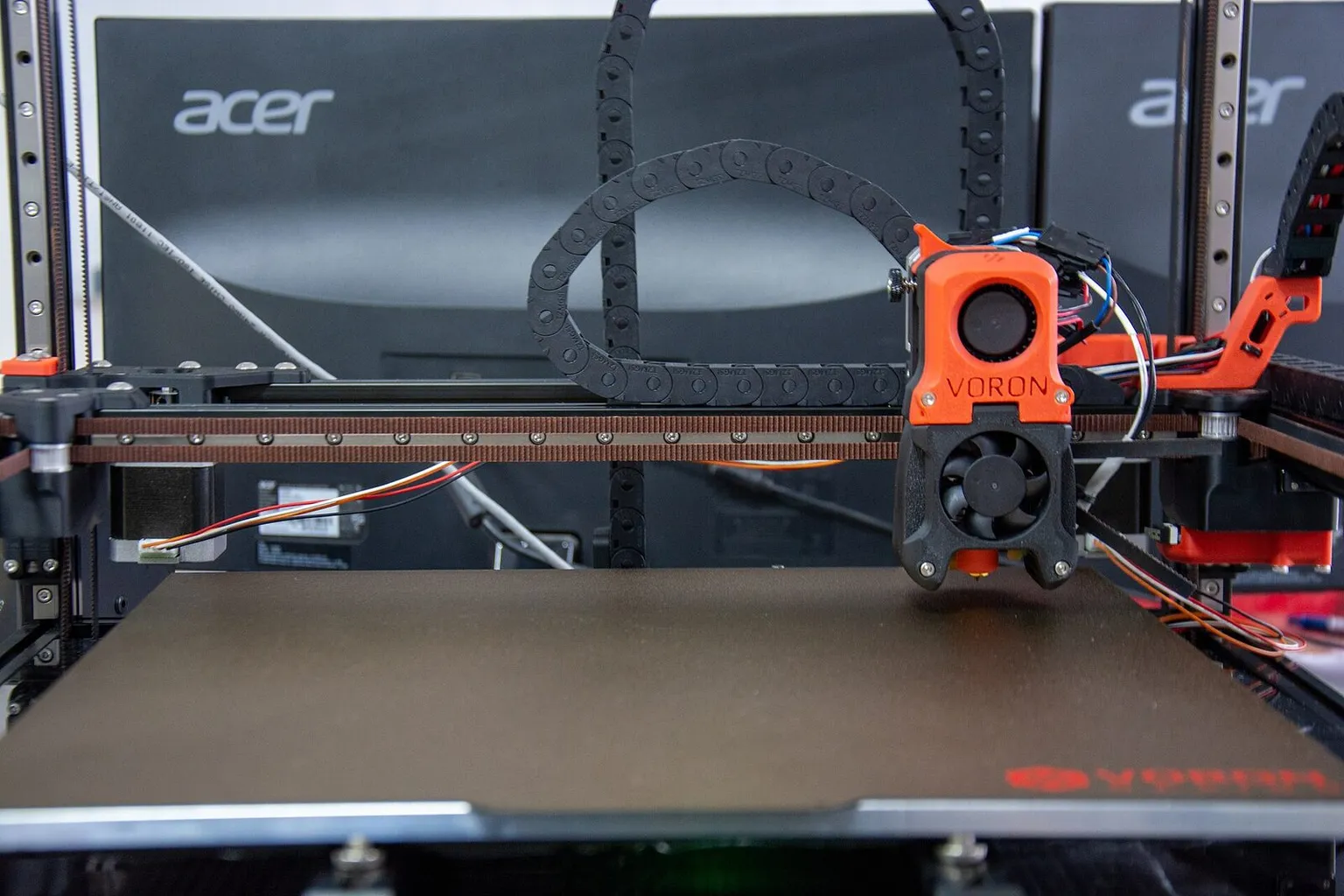 A Voron 3D printer seen from the front, its orange toolhead above a black textured build plate