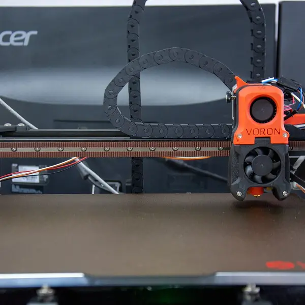 A Voron 3D printer seen from the front, its orange toolhead above a black textured build plate