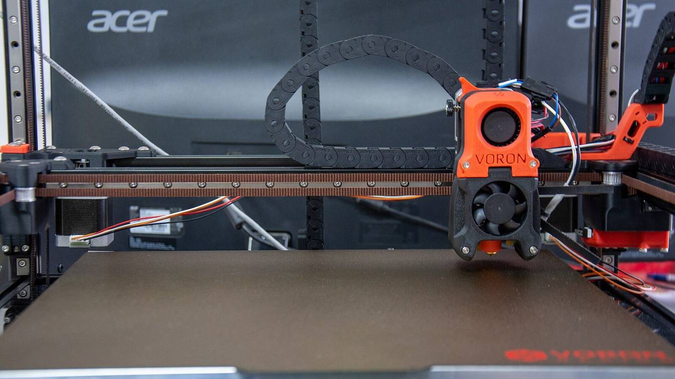 A Voron 3D printer seen from the front, its orange toolhead above a black textured build plate