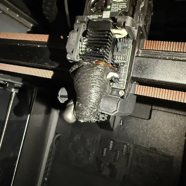 A printer hotend encased in a blob of grey plastic after a failed print