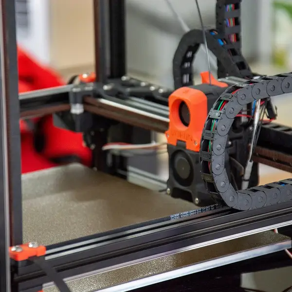 Inside a Voron printer frame, the orange toolhead on its gantry with the cable chain coiled above