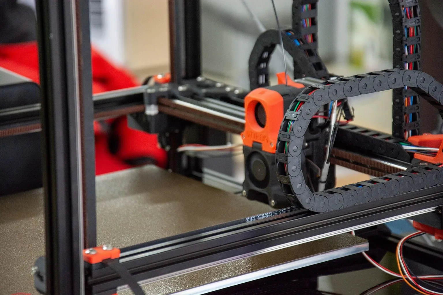 Inside a Voron printer frame, the orange toolhead on its gantry with the cable chain coiled above