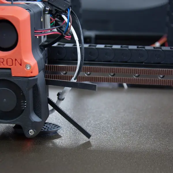 An orange Voron toolhead with its cooling fans, low over a textured build plate