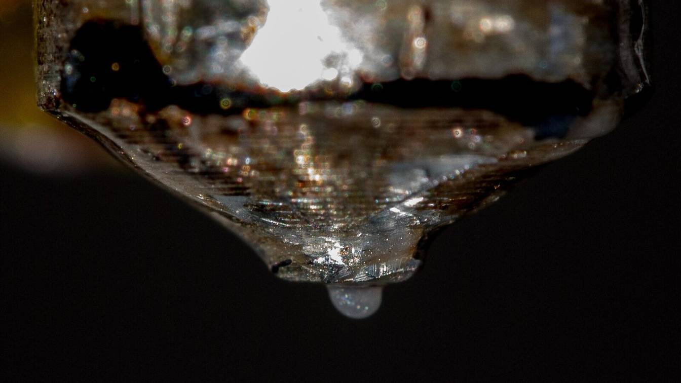 Close-up of a 3D printer nozzle with a bead of molten plastic hanging from its tip