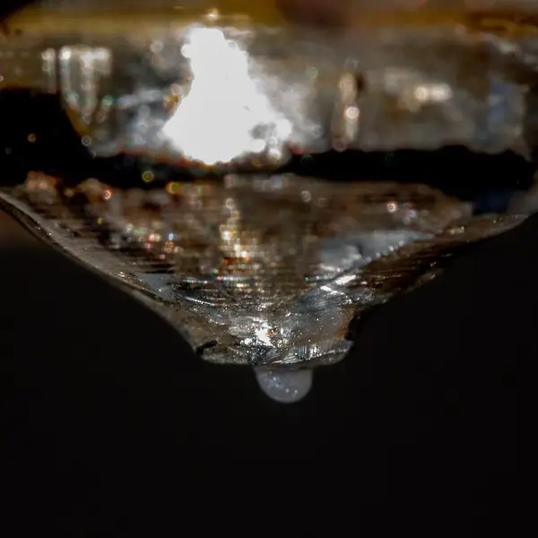 Close-up of a 3D printer nozzle with a bead of molten plastic hanging from its tip