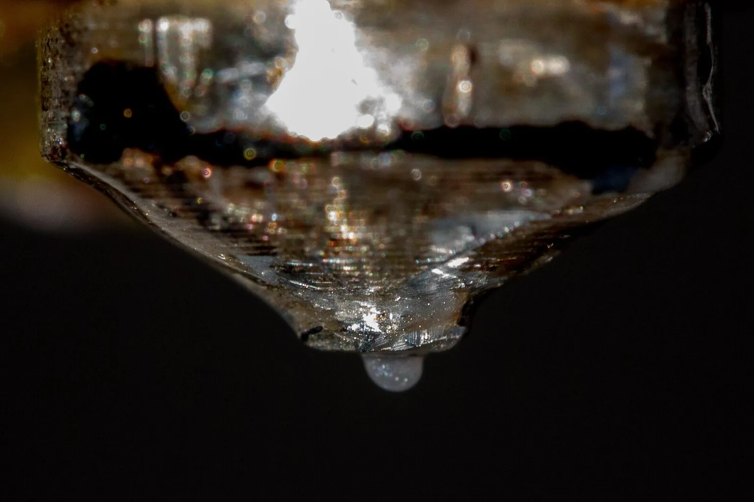 Close-up of a 3D printer nozzle with a bead of molten plastic hanging from its tip
