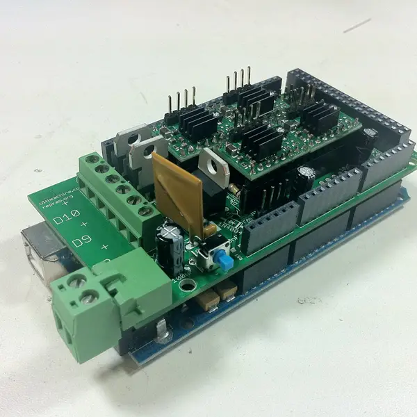A RAMPS 3D printer controller board stacked on an Arduino Mega, with four stepper driver modules, heatsinks and green screw terminals, on a white desk