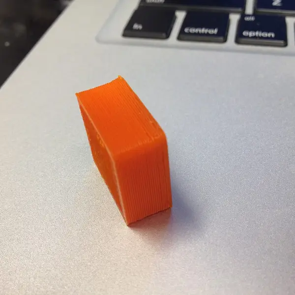 A small orange 3D-printed test block lying on a laptop