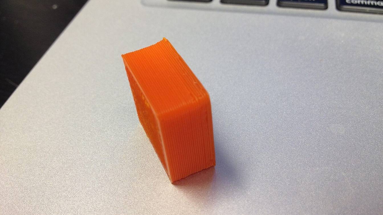 A small orange 3D-printed test block lying on a laptop
