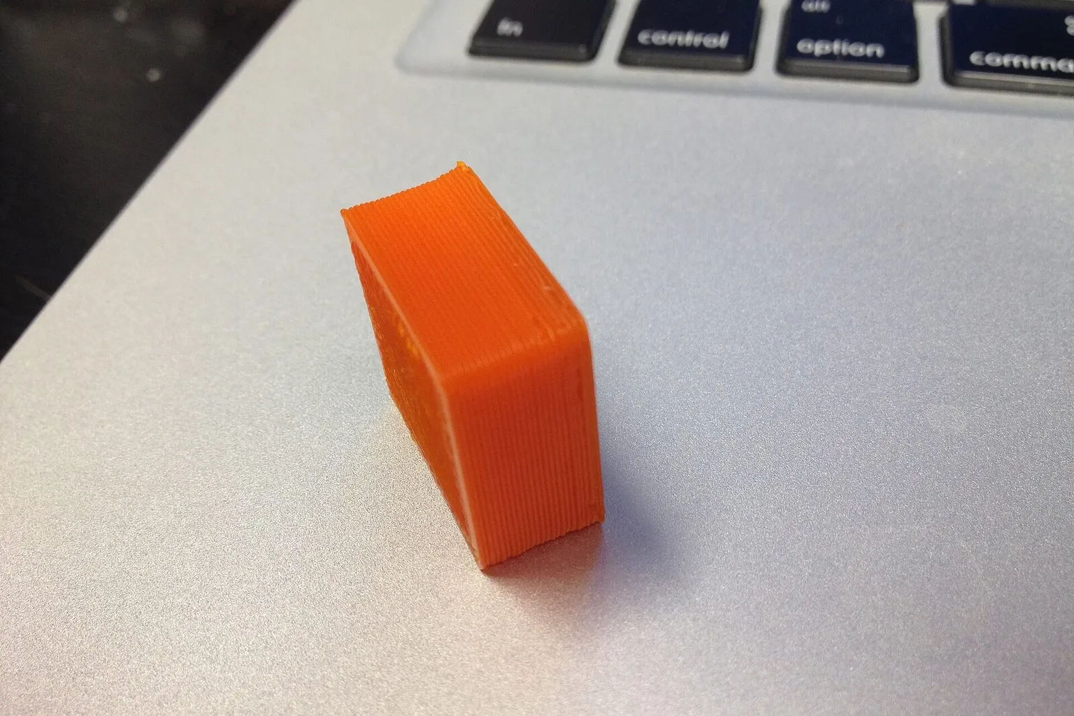 A small orange 3D-printed test block lying on a laptop