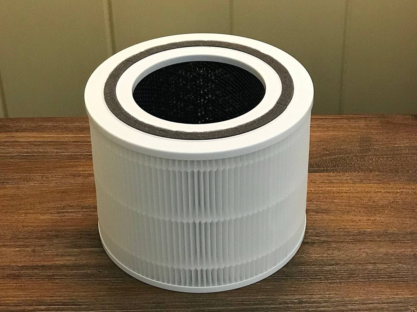 A round air purifier filter standing on a wooden table: white pleated HEPA media on the outside and a black activated carbon layer lining the inside
