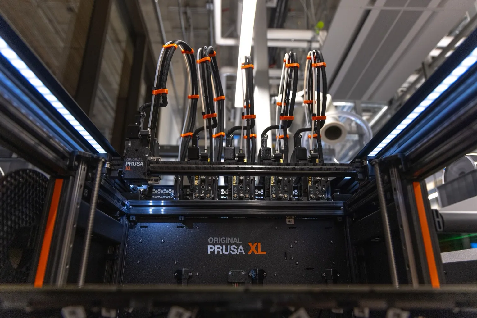 Looking into an open Prusa XL from the front: the tool-changer carriage on the left of the gantry and five toolheads parked in their docks along the back, with bundled cables rising from each