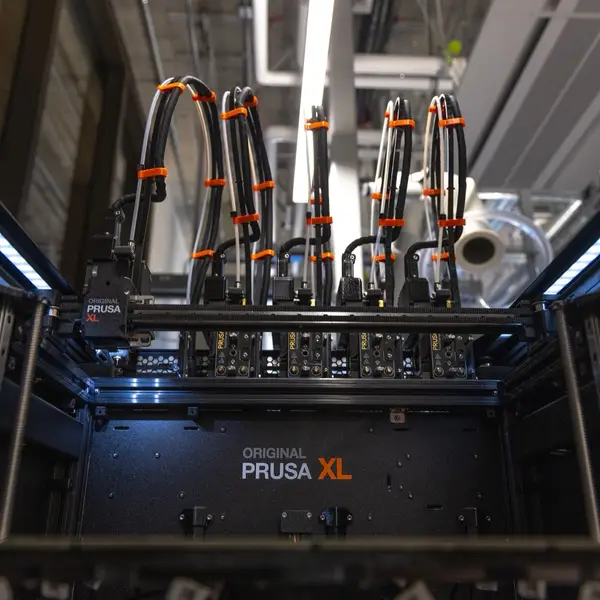 Looking into an open Prusa XL from the front: the tool-changer carriage on the left of the gantry and five toolheads parked in their docks along the back, with bundled cables rising from each
