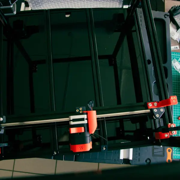 Top-down view of a Voron 2.4 frame under assembly, with a red and black toolhead on the X gantry above the empty bed area