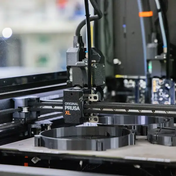 Close-up inside a Prusa XL: the active toolhead on the X gantry above round black prints on the bed, with more toolheads parked in their docks at the back