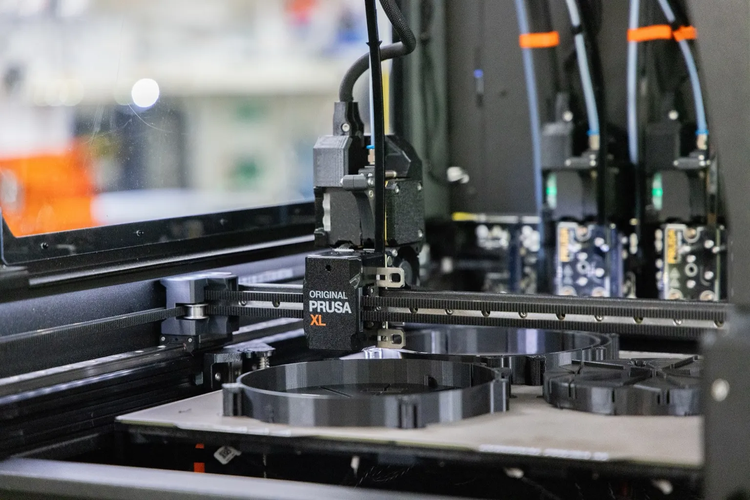 Close-up inside a Prusa XL: the active toolhead on the X gantry above round black prints on the bed, with more toolheads parked in their docks at the back