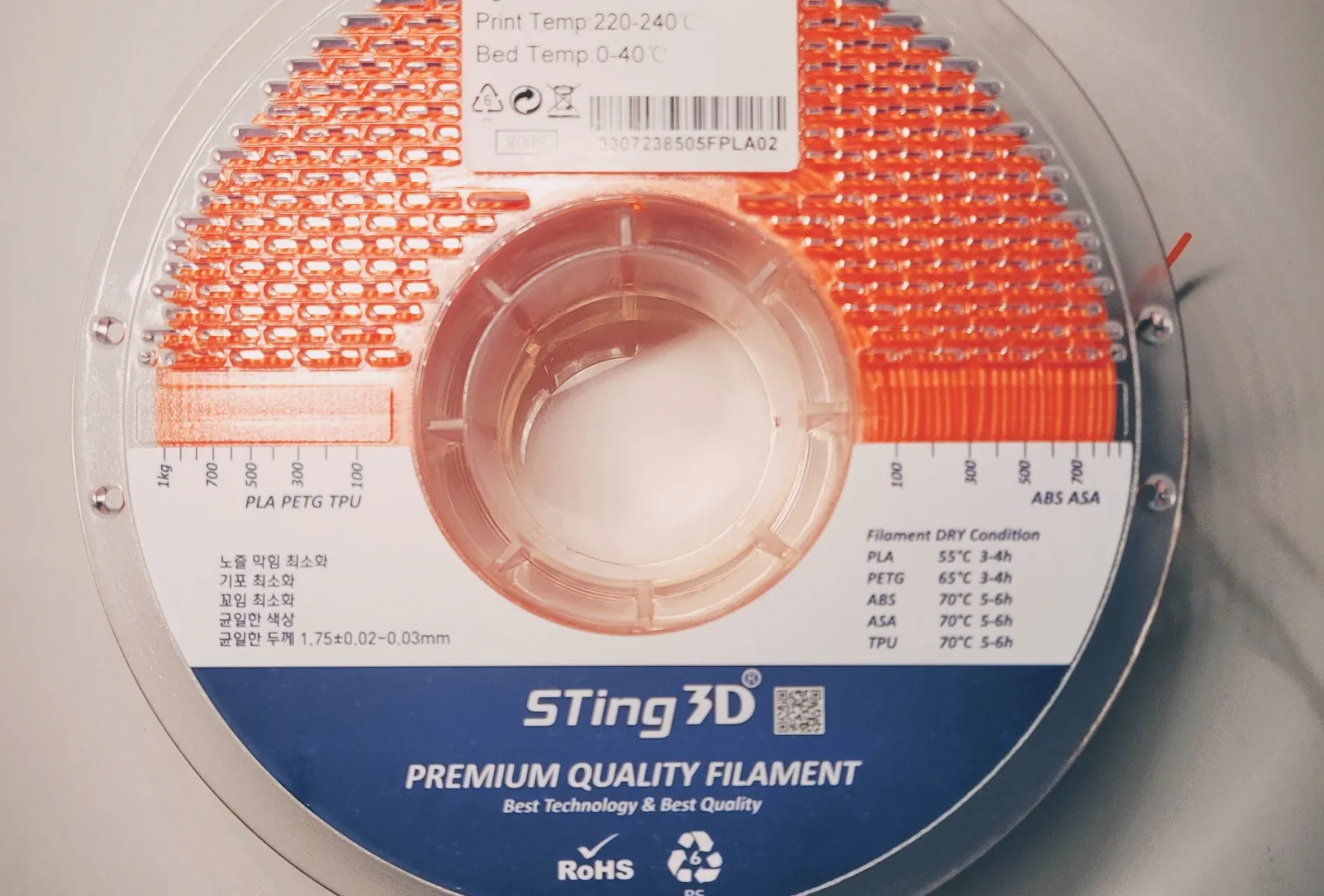 A clear plastic spool of orange flexible filament with a label listing print and bed temperatures, on a marble surface