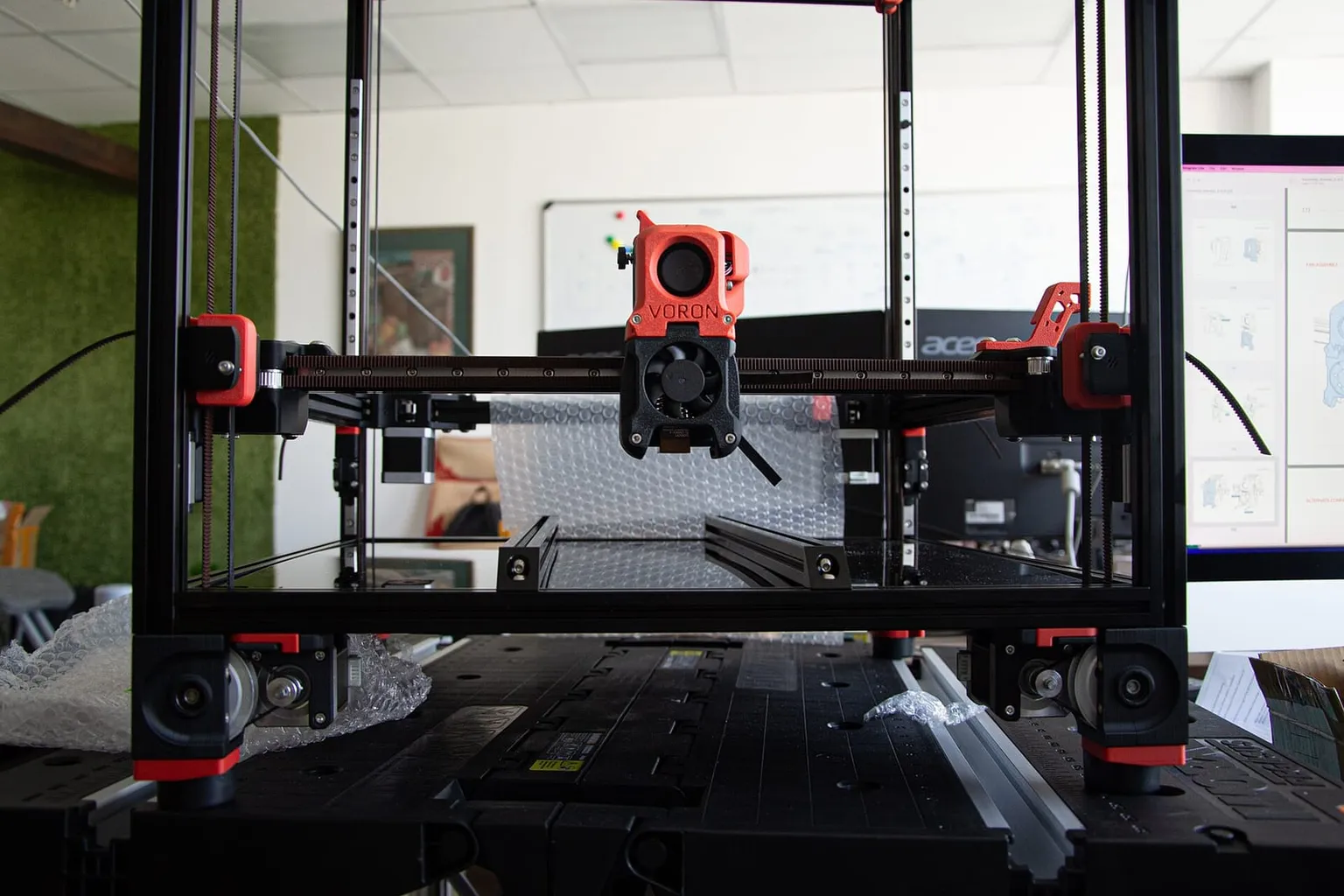 A Voron printer during assembly, its toolhead on the gantry above the bed frame