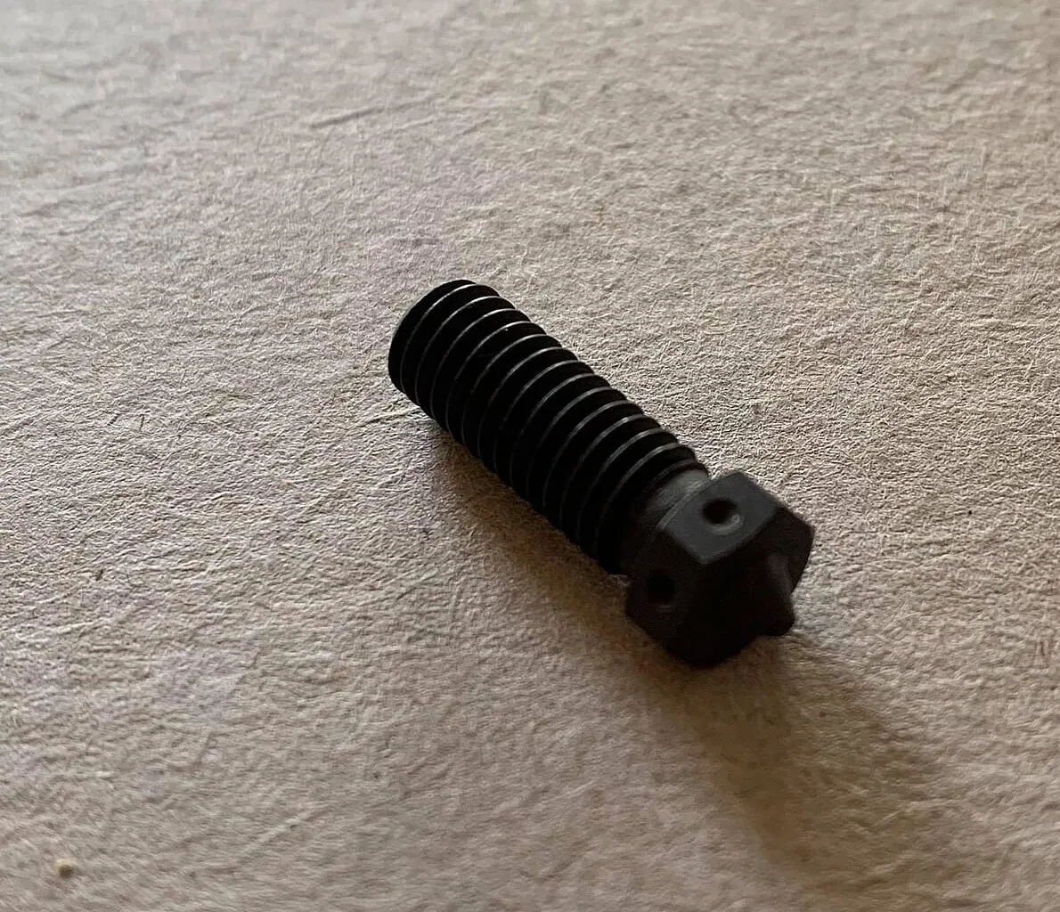 A hardened steel 0.4 mm nozzle lying on a flat surface
