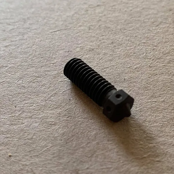 A hardened steel 0.4 mm nozzle lying on a flat surface