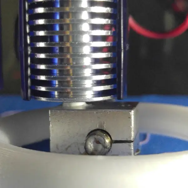 Close-up of an E3D V6-style hotend: a finned aluminum heatsink above a heater block with a clamp screw, inside a white printed ring-shaped fan duct