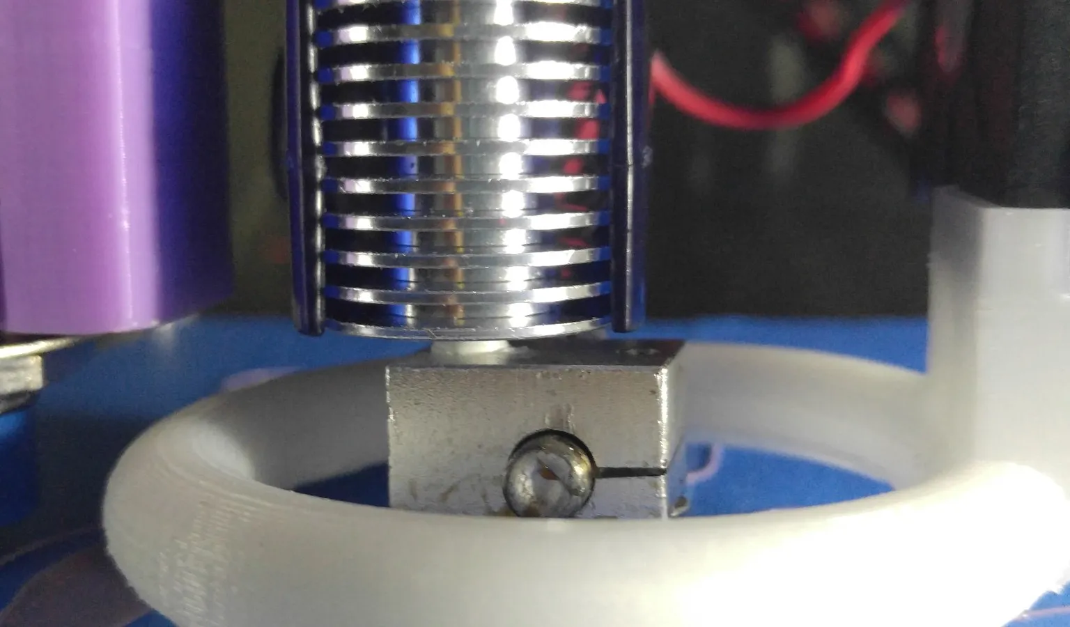 Close-up of an E3D V6-style hotend: a finned aluminum heatsink above a heater block with a clamp screw, inside a white printed ring-shaped fan duct