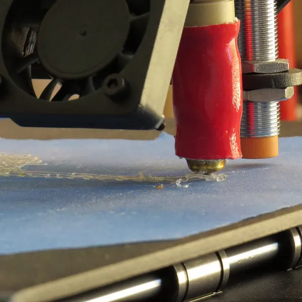 A nozzle laying down the first layer on blue tape, with an inductive probe beside it